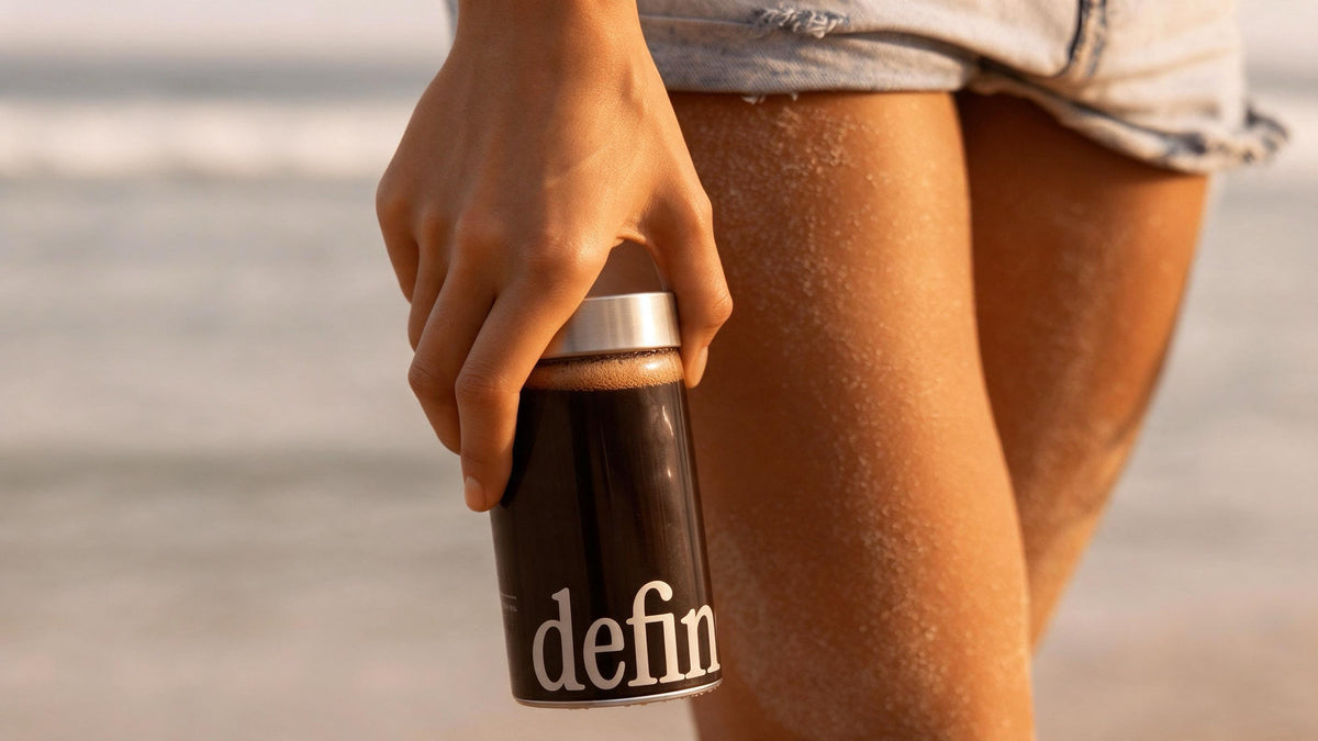 Hand holding a glass bottle of defined black coffee on the beach