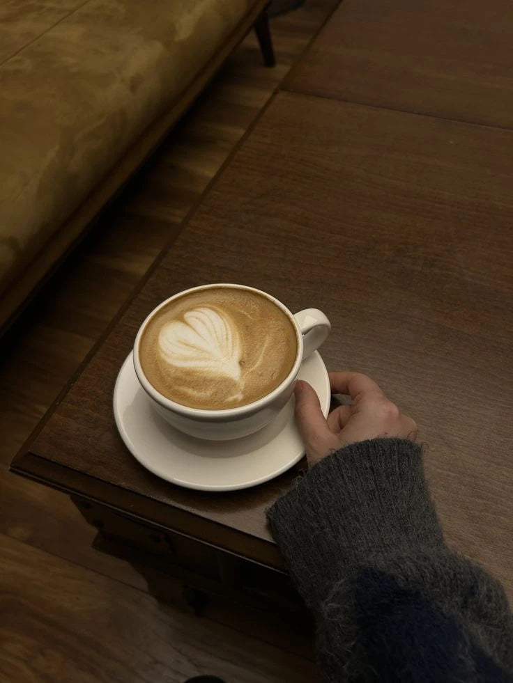 Latte with heart latte art in a white cup, a hand resting beside the saucer
